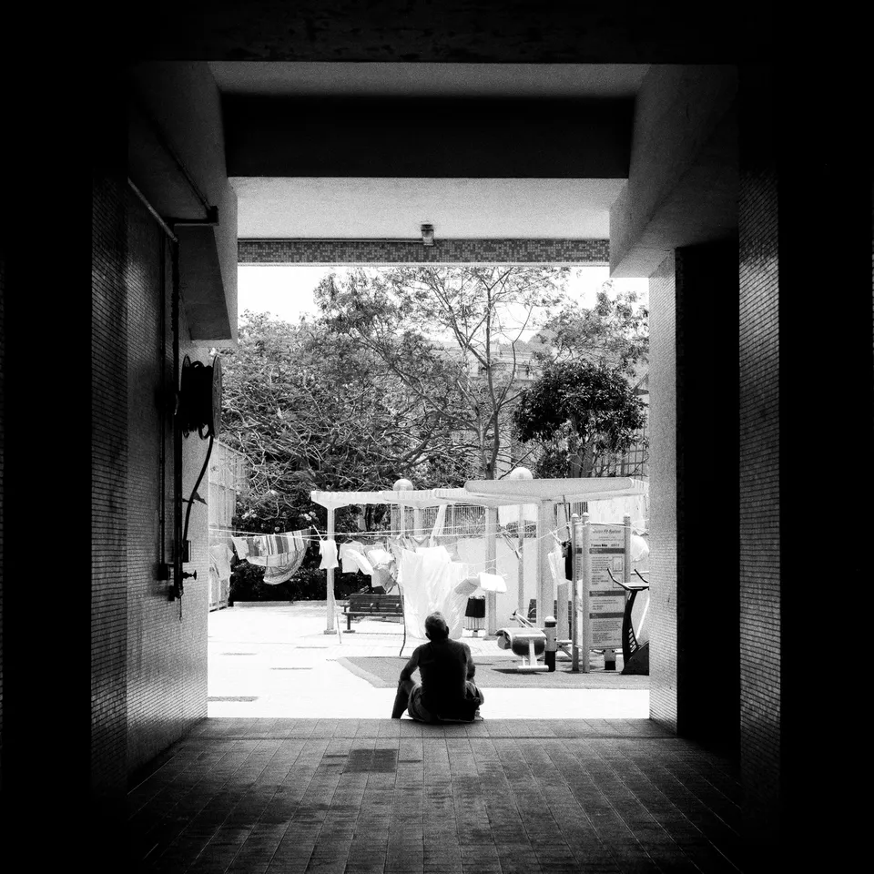 Back of an elderly man sitting on the step of an indoor area, looking outside