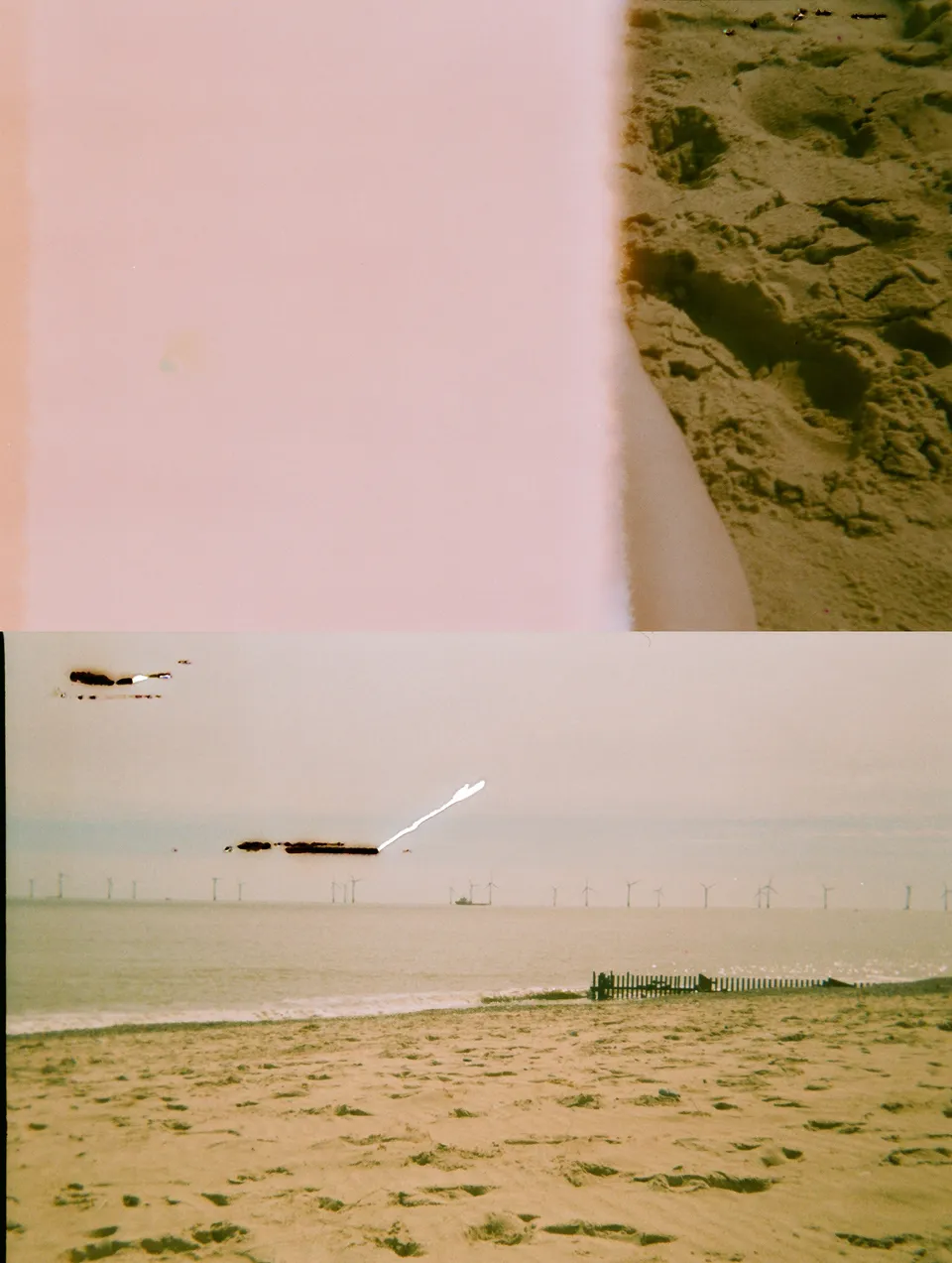 Upper half: 1/3 of the shot is visisble with someone's leg. Lower half: view from a beach where a wind farm can be seen from a distance.