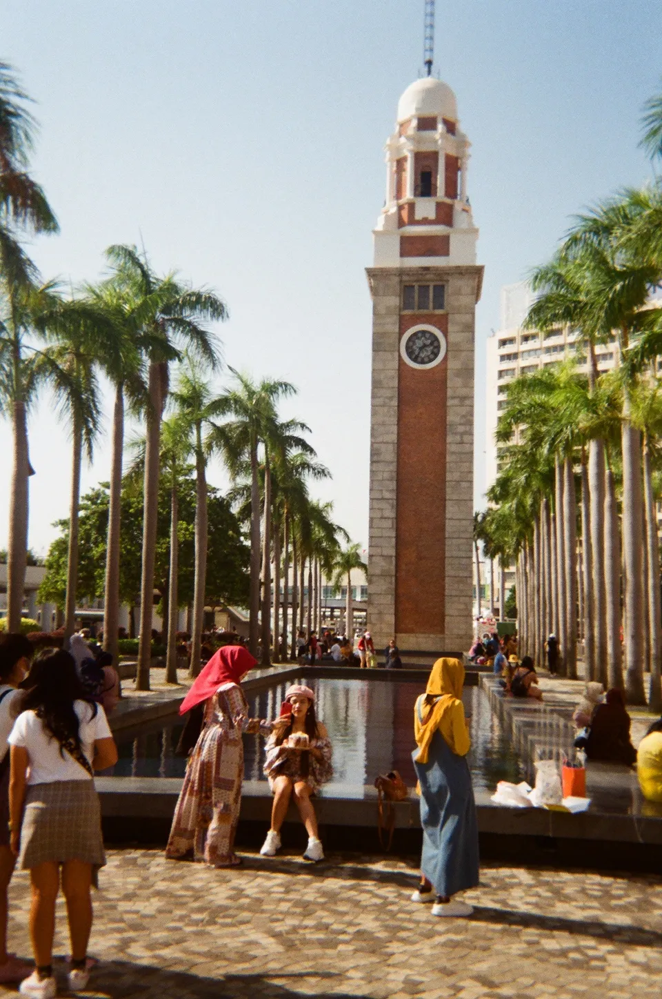 Color photo of lady holding up a birthday cake in front of the clock tower in Tsim Sha Tsui
